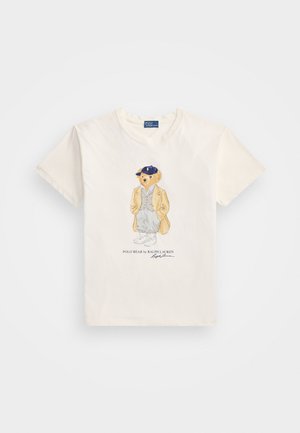 Kreemi puuvillane T-särk, millel on graafiline illustratsioon karust jakis ja mütsiga, ning all tekst "POLO BEAR by RALPH LAUREN."