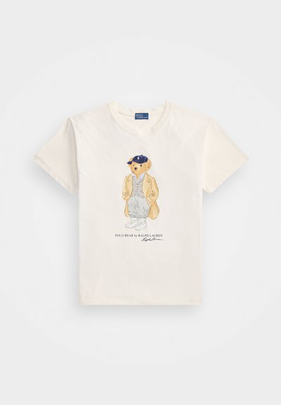 Kreemist puuvillast T-särki, millel on graafiline joonistus karust, kes kannab jakki ja mütsi, all tekstiga "POLO BEAR by RALPH LAUREN."