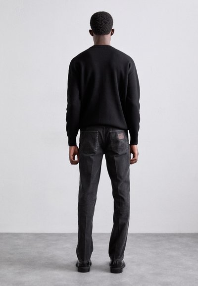 Black sweater and dark gray jeans viewed from the back. The jeans feature a brown label patch and a straight-leg design. Smooth texture.