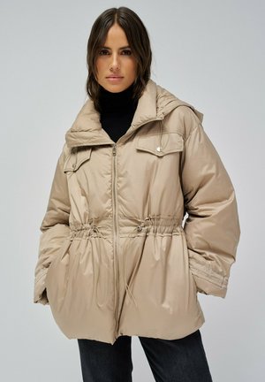 Chaqueta acolchada beige con capucha, cintura ajustable con cordón, bolsillos frontales y cierre de cremallera. Acabado de tela suave con un ligero brillo.