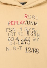 Sweat à capuche beige avec une texture douce, comportant un texte imprimé en rouge et gris, y compris le nom de la marque "REPLAY" et divers numéros.