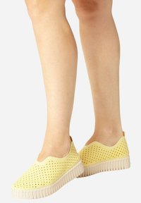 Yellow perforated slip-on shoes with a flexible upper and a textured white rubber sole, featuring a low profile and a rounded toe.