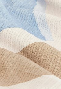 Vícebarevná textilie s modrými, béžovými a krémovými sekcemi v texturovaném tkaní. Obsahuje diagonální vzory vytvářející kontrast v barvách.