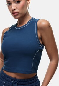 Top corto a righe blu con scollatura tonda, cuciture in contrasto e design senza maniche, abbinato a pantaloni svasati blu scuro.