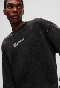 Sort, oversized sweatshirt med en slidt tekstur, prydet med et hvidt broderet logo "KARL LAGERFELD JEANS" på brystet. Rund halsudskæring.