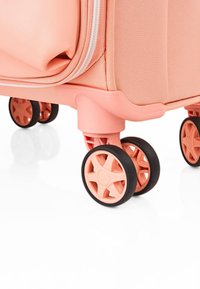 Maleta color melocotón con una superficie texturizada, doble cremallera y cuatro ruedas multidireccionales con bandas de goma gris.