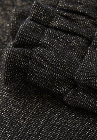 Schwarzer strukturierter Stoff mit goldenen metallischen Fäden, der ein gestricktes Muster und ein gerafftes Design zeigt. Weich mit sichtbaren Nähdetails.