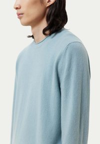 Hellblaues Langarmshirt mit Rundhalsausschnitt und weichem, strukturiertem Stoff. Der Schnitt ist lässig, mit minimal sichtbaren Nähten.