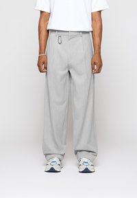 Pantalon gris à jambes larges avec plis et détail anneau métalique à la taille, assorti à des baskets blanches avec des accents bleus.