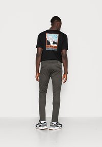 Black short-sleeve t-shirt with graphic design, featuring mountains and trees, paired with olive green pants and black sneakers.