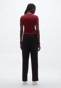 Piros, rövid ujjú felső kerek nyakkivágással, laza fekete nadrággal párosítva. A ruházat sima textúrájú és kényelmes szabású, alkalmas mindennapi viseletre.