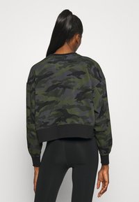 Felpa corta in verde scuro e motivo camouflage nero. Presenta maniche lunghe, polsini a coste e una vita nera uniforme.