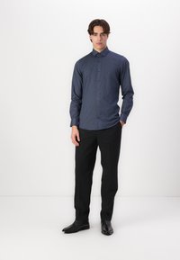 Navy button-up shirt with subtle dot pattern, long sleeves, and a classic collar; paired with dark trousers and black shoes.
