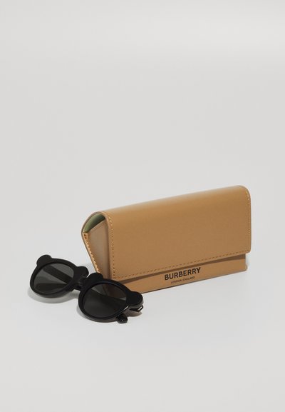 Crne sunčane naočale s naglascima u obliku medvjeda pored smeđeg kožnog etuija, u kojem je urezano "BURBERRY" crnim slovima.