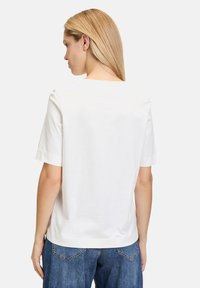 Weißes Baumwoll-T-Shirt mit kurzen Ärmeln, Rundhalsausschnitt und lässiger passform. Der Rücken hat einen Standardschnitt ohne zusätzliche Details.