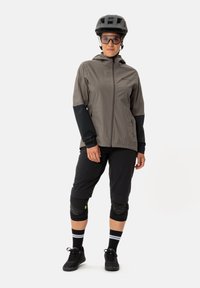 Giacca leggera grigia con maniche nere, abbinata a pantaloni corti neri fino al ginocchio, ginocchiere e sneaker nere. Indossata con un casco nero.