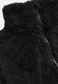 Zwarte fleece vest met een hoge kraag, ritssluiting en een gestructureerd, pluizig oppervlak met een zachte, harige feel.