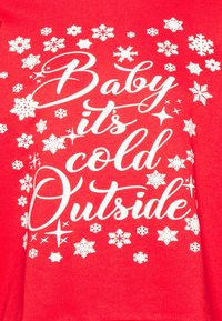 Felpa rossa con testo bianco che riporta "Baby it's cold Outside" circondato da vari grafiche di fiocchi di neve. Tessuto morbido e testurizzato.