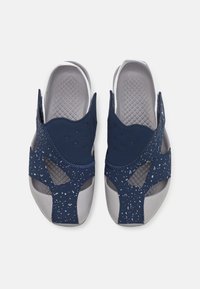 Pár tmavě modrých a šedých gumových sandálů s otevřenými prsty a skvrnitým vzorem na popruzích, zobrazených shora na bílém pozadí.