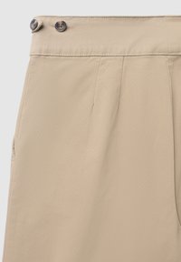 Beige Hosen mit flachem Bund, zwei Fronttaschen und zwei dekorativen Knöpfen am Bund. Glattes Gewebe mit einer dezenten Textur.