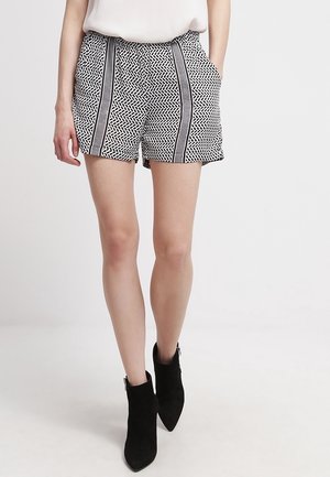 Pantaloni corti a righe bianchi e neri con un design geometrico, caratterizzati da una vita alta e strisce laterali in contrasto, abbinati a stivaletti neri alla caviglia.