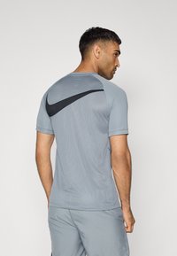 Hallide hallide Nike sportpaita lühikeste varrukatega, mis on varustatud hingava tekstuuriga ja musta logo aktsendiga seljaosas.