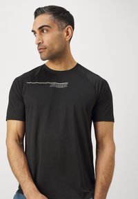 Zwart atletisch T-shirt met korte mouwen, een ronde halslijn en een wit logo op de borst, gemaakt van een lichtgewicht, glad materiaal.