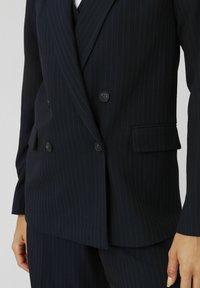 Blazer double boutonnage bleu marine foncé avec des rayures verticales, comportant deux boutons, des poches latérales et une texture lisse. Coupe ajustée.