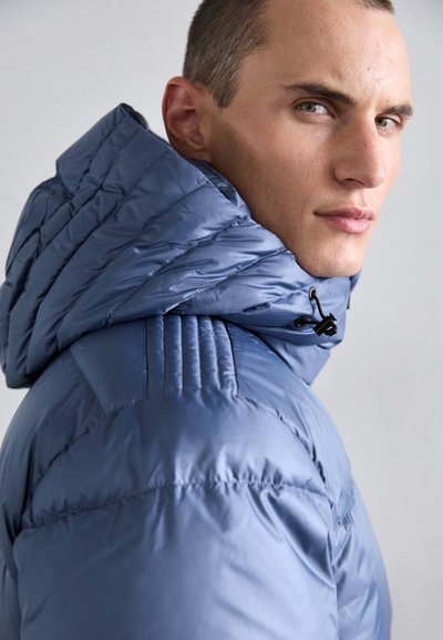 Blaues Steppjacke mit hohem Kragen und Kapuze. Der Stoff ist glänzend und gepolstert, mit horizontalen und vertikalen Nähmustern.