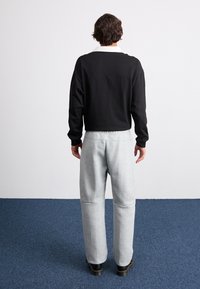 Pulpă neagră scurtă cu mâneci lungi, asortată cu pantaloni scurți gri deschis cu un croi relaxat. Modelul stă în fața unui fundal neutru.