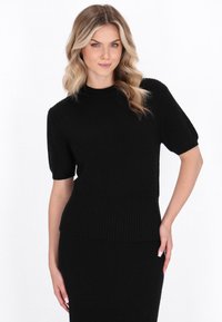 Kortærmet sort ribstrikket sweater med høj hals og tætsiddende talje, der har et tekstureret mønster og en strømlinet silhuet.