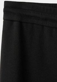 Gros plan sur une ceinture en tissu noir avec des coutures visibles et un matériau doux et texturé.