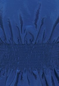 Tessuto blu con una texture liscia, caratterizzato da un elastico arricciato in vita che crea un effetto volant sotto.