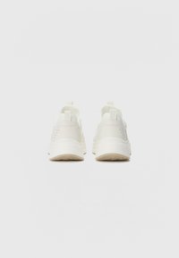 Weiße Sportschuhe mit einem aerodynamischen Design, das mit durchlöcherten Details an der Ferse und einer strukturierten Gummisohle ausgestattet ist.