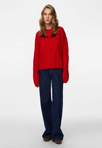 Red knitted sweater with a boxy fit and wide sleeves, paired with dark blue flared denim jeans. Simple and textured patterns on sweater.