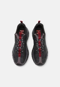 Chaussures de sport noires et grises avec dessus en mesh, accents rouges, lacets à motif, semelle texturée, et une languette à l'arrière du talon.