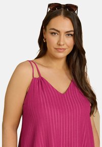 Fuchsia ärmlös topp med tunna justerbara spännen och V-ringning. Strukturen i tyget har vertikal ribbing för extra detalj.