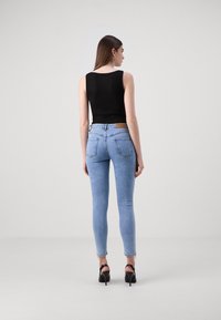 Fekete bordás trikó, amelyet világoskék skinny farmernadrággal párosítanak. A farmernadrág magas derékkal, hátsó zsebekkel és enyhén foszlott szegéllyel rendelkezik. Fekete magassarkú.