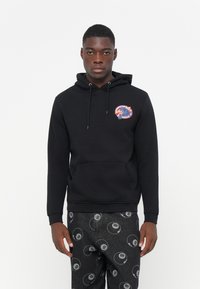 Zwarte hoodie met een voorzak en een capuchon met trektouw. Voorzien van een gekleurd grafisch patroon op de borst. Gekoeld met een patroon van donkere broeken.
