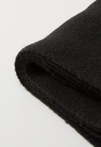 Tissu en laine noire, texture douce, plié avec des fibres visibles, sans motifs ni accessoires. Bords propres, finition mate, aspect léger.