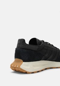 Černá teniska s texturovanou černou látkou a hladkými koženými prvky. Má béžovou gumovou podrážku a vyšívané logo na patě.