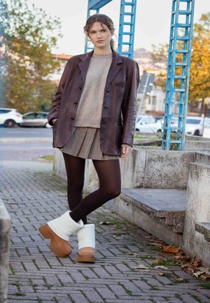 Brown leather blazer over a gray sweater, striped mini skirt, and dark tights. White and brown chunky boots. Urban setting with pavement.