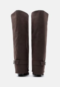 Καφέ λαστιχένιες μπότες μέχρι το γόνατο με λείο υφή, διακοσμημένες με ασημένιες αγκράφες και ελαφριά τακούνια για επιπλέον σταθερότητα.