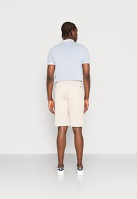 Lyseblå polo-shirt og beige shorts i en klassisk pasform. Shortsene har en baglomme. Hvide sneakers med marineblå detaljer fuldender looket.