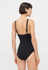 Black one-piece swimsuit with adjustable straps, a low back design, and smooth texture. Features minimalistic style and clean lines.