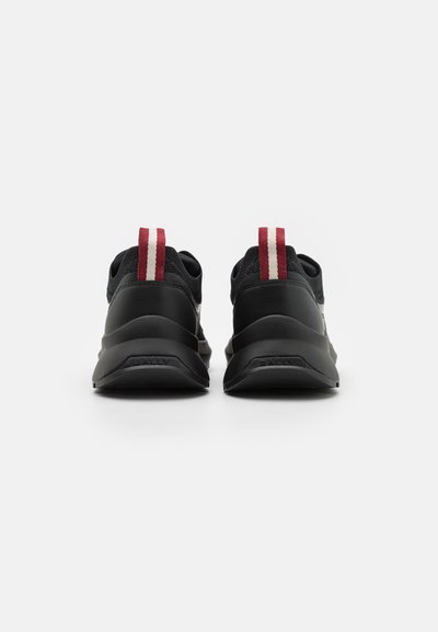 Sneakers neri con una parte superiore texturizzata, suola spessa e accenti rossi a strisce sul tallone. Marchio visibile nell'area della suola posteriore.
