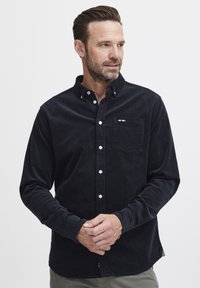 Marine knapper skjorte laget av kordfløyelstoff, med en brystlomme med en liten rød, hvit og blå logodetalj. Lange ermer.