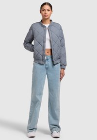 Grijze gewatteerde bomberjack met een ronde kraag, voorrits en geribde mouwen, gecombineerd met lichtblauwe high-waisted denim jeans.