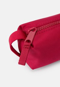 Trousse à crayons en tissu rouge avec une surface texturée, dotée d'une fermeture éclair assortie et d'une petite poignée pour un transport facile.