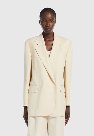 Beige skræddersyet blazer med spidse klapper, to forlommer og en let oversized pasform, lavet af glat, letvægtigt stof.